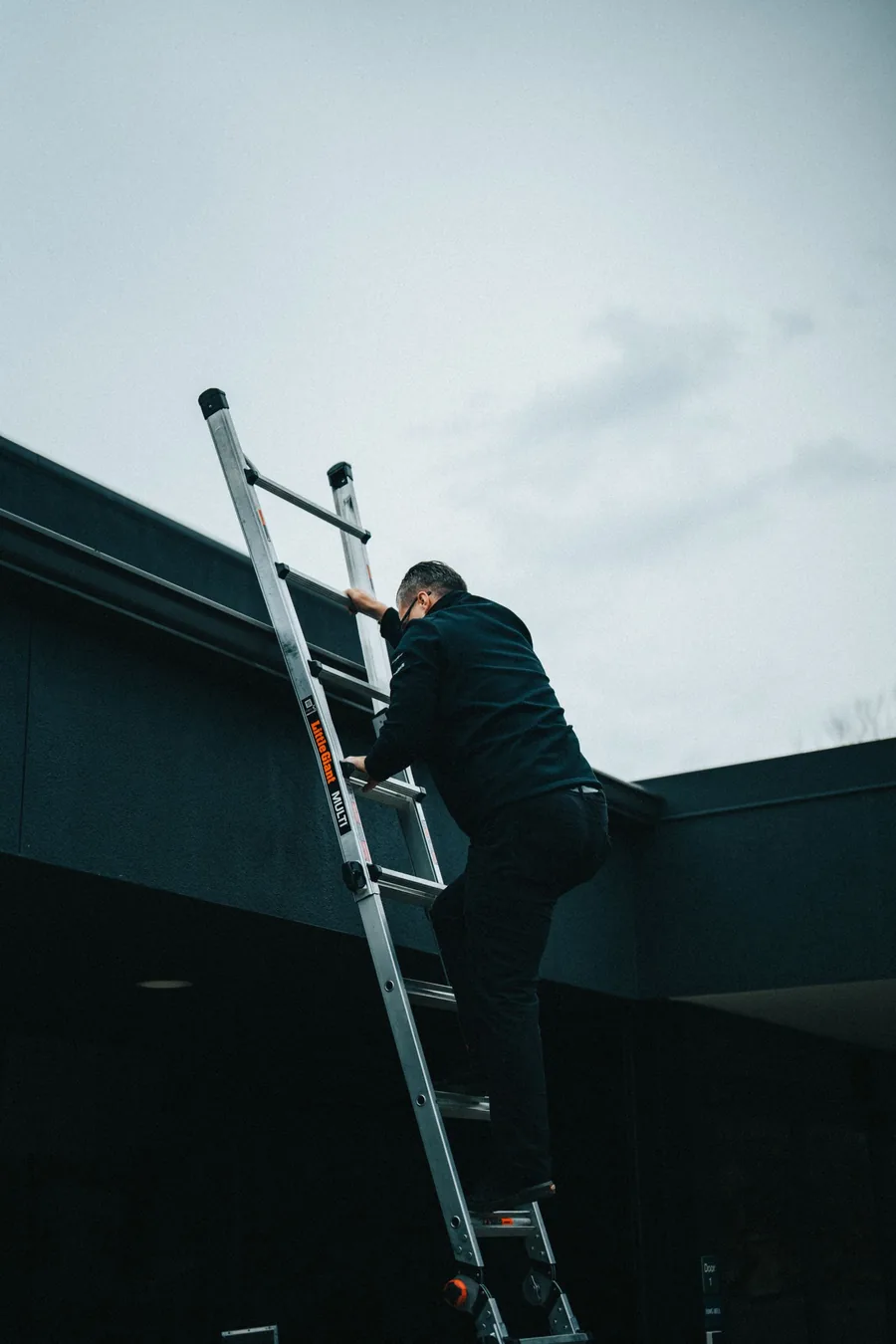 Maintenance worker climbing a ladder to the roofline